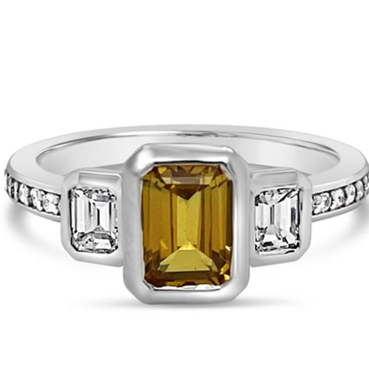 Crafted of 18k white gold, this trilogy ring features a unique yellow beryl stone. Highlighted with a set of baguette diamonds & grain set shoulder diamonds.